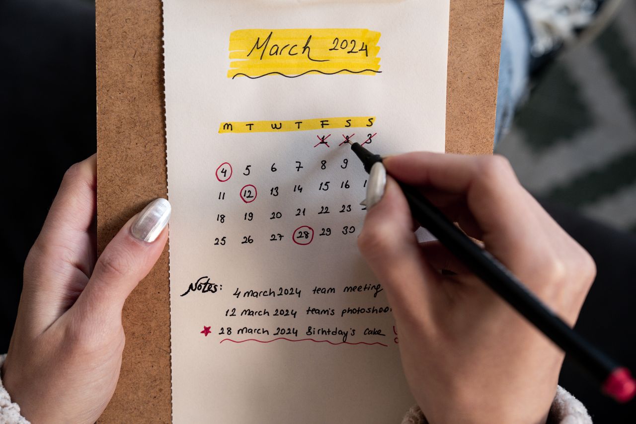 Close-up of a woman's hands organizing a planner for March 2024 with handwritten notes and highlights.