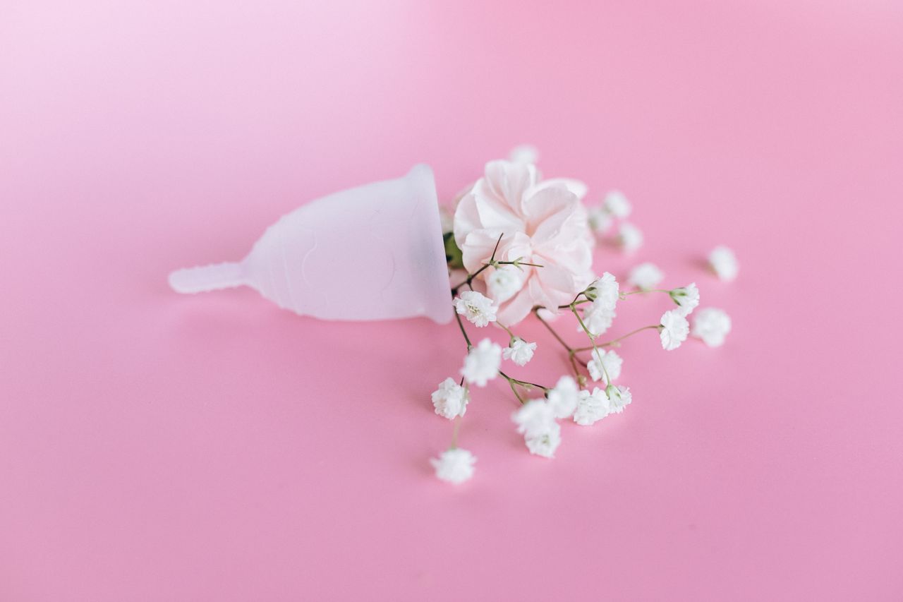 A silicone menstrual cup placed alongside baby's breath flowers on a soft pink background.