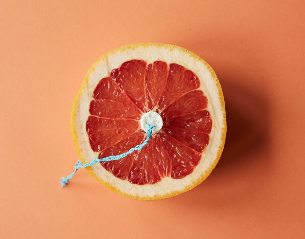 Top view of feminine tampon placed in half of fresh ripe grapefruit against orange background in studio