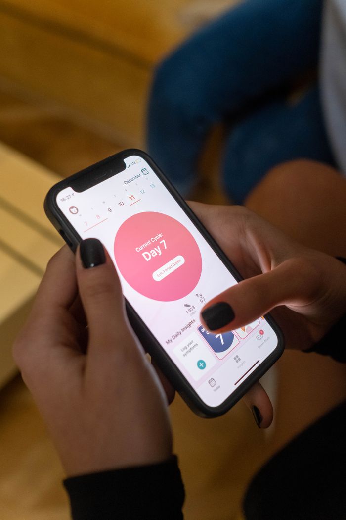 Close-up of a woman using a menstrual tracking app on her smartphone indoors.