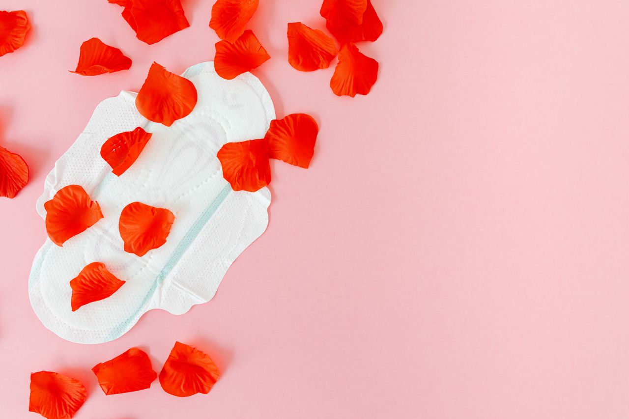 A feminine hygiene pad surrounded by red petals on a pink surface, symbolizing menstruation.